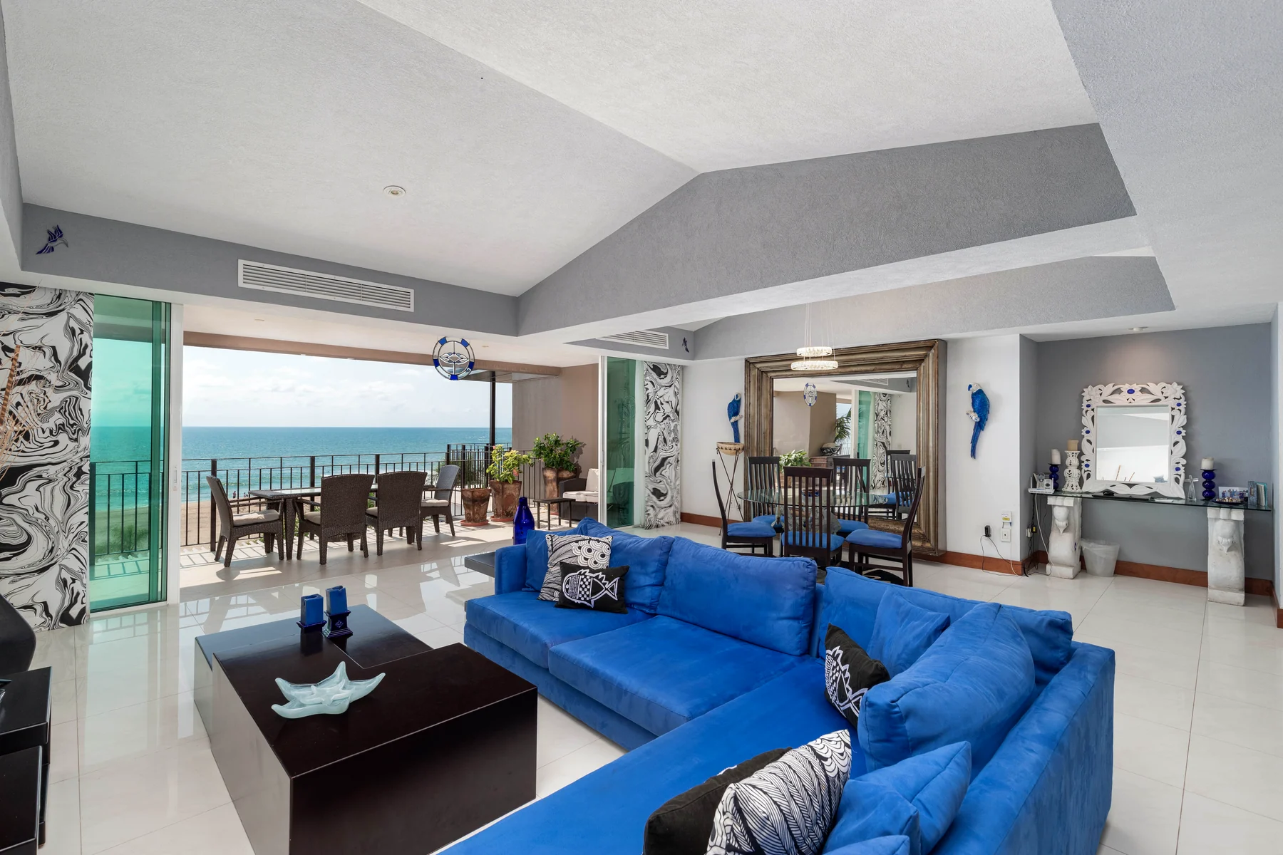 Main living room with blue sofa and the wall of glass open to the terrace and the sea